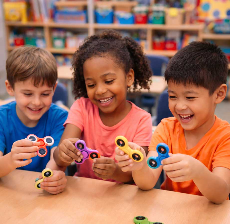 children_playing_fidget Three children sitting at a table playing with fidget spinners